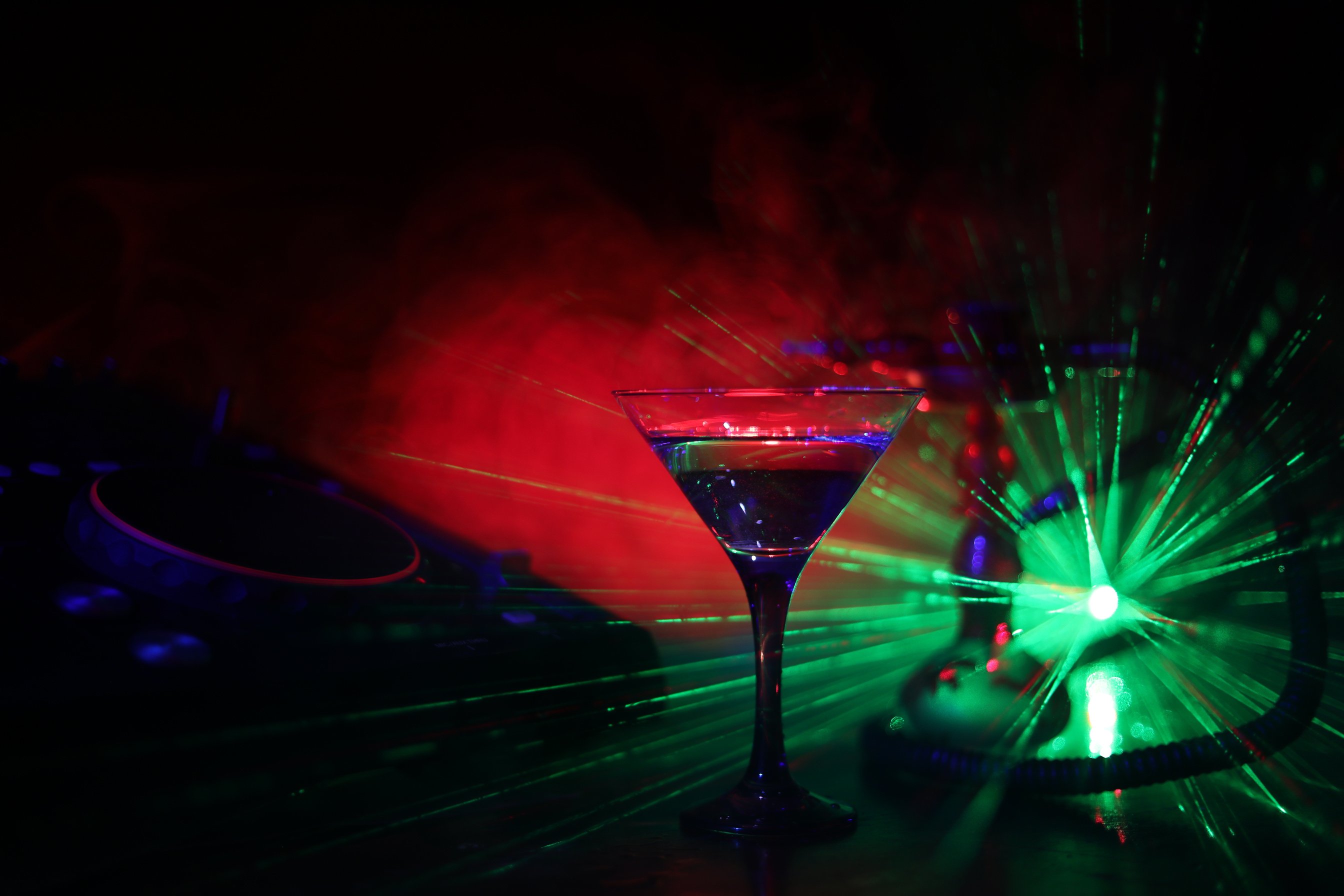 Glass with martini with olive inside on dj controller in night club. Dj Console with club drink at music party in nightclub with disco lights.